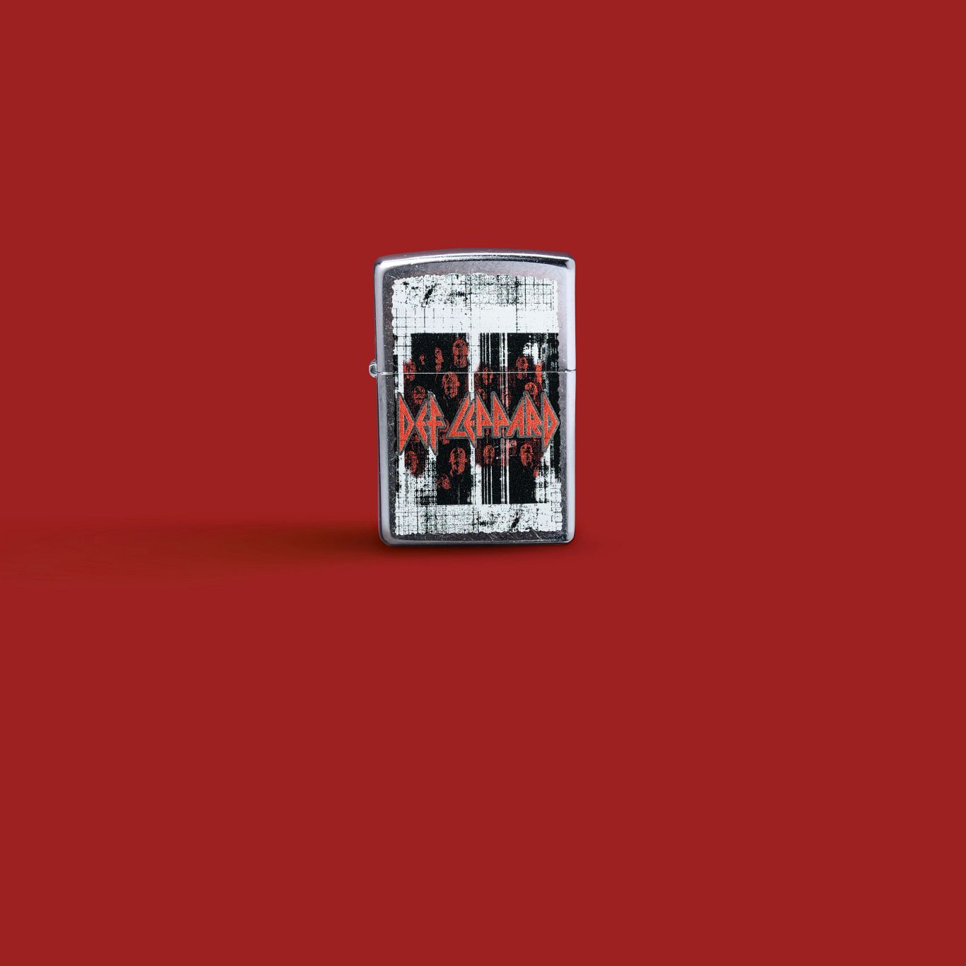Lifestyle image of Zippo Def Leppard Logo Design Street Chrome Windproof Lighter standing against a red background.