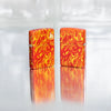 Lifestyle image of two Zippo Fire Design 540 Tumbled Brass Windproof Lighters on a reflective glass block background.