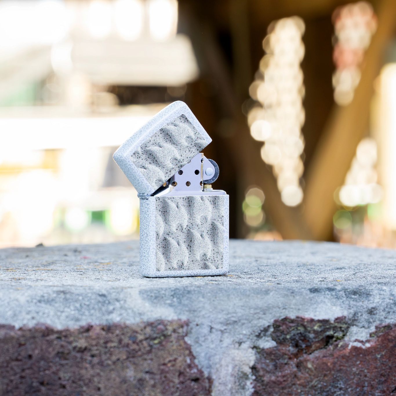 Lifestyle image of Zippo Frozen Flames Design Glacier Windproof Lighter standing on a brick surface with blurred background.