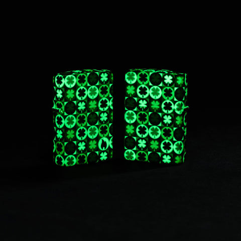 Lifestyle image of two Zippo Clover Design Glow in the Dark Green Matte Windproof Lighters glowing in the dark.