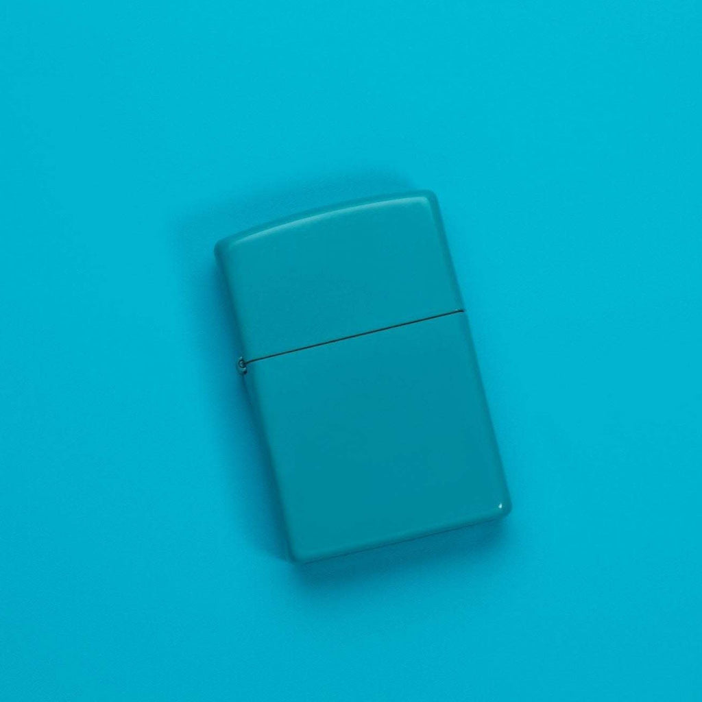 Lifestyle image of Classic Flat Turquoise Windproof Lighter laying on a turquoise surface