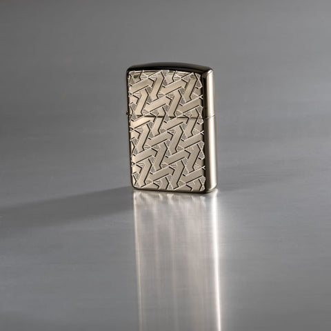 Lifestyle image of Armor Geometric Weave High Polish Black Ice Windproof Lighter standing on a reflective surface