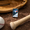 Lifestyle image of MLB® Toronto Blue Jays™ Street Chrome™ Windproof Lighter laying on a baseball field with a glove, ball, and bat.