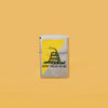 Lifestyle image of Dont Tread On Me® Flag Design Brushed Chrome Windproof Lighter standing in a yellow background.