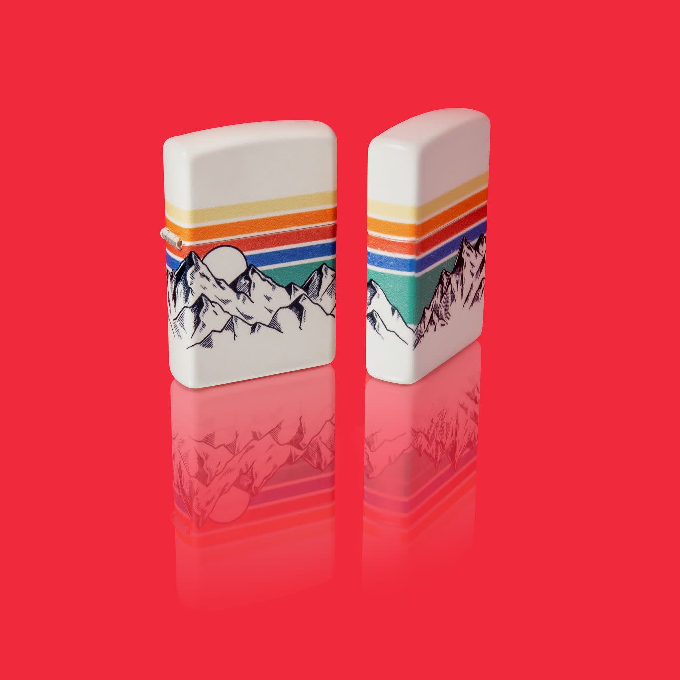 Glamour shot of two Zippo Mountain Design 540 Color Windproof Lighters standing in a red scene.