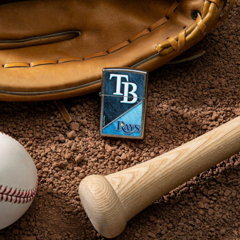 Lifestyle image of MLB® Tampa Bay Rays™ Street Chrome™ Windproof Lighter laying on a baseball field with a glove, ball, and bat.