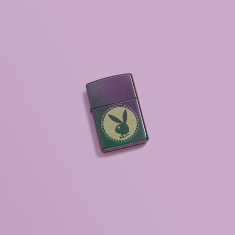 Lifestyle image of Playboy Engraved Rabbit Head Iridescent Windproof Lighter laying on a pink background.