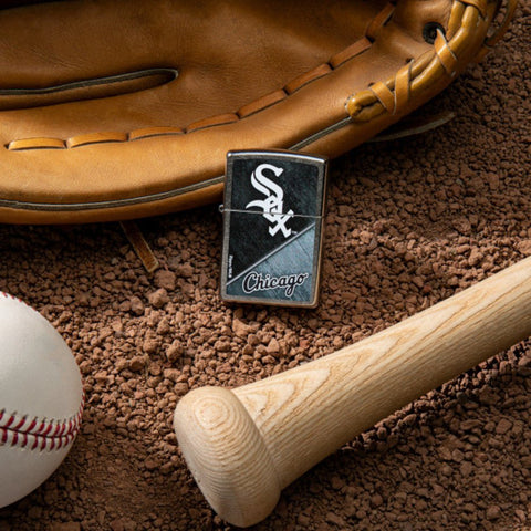 Lifestyle image of MLB® Chicago White Sox™ Street Chrome™ Windproof Lighter laying on a baseball field with a glove, ball, and bat.