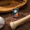 Lifestyle image of MLB® Houston Astros™ Street Chrome™ Windproof Lighter laying on a baseball field with a glove, ball, and bat.