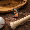 Lifestyle image of MLB® San Francisco Giants™ Street Chrome™ Windproof Lighter laying on a baseball field with a glove, ball, and bat.