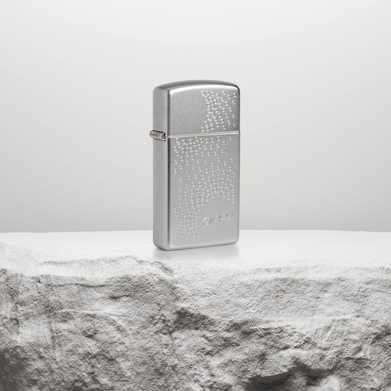 Lifestyle image of SlimÂ® Zippo Dot Design Satin Chrome Windproof Lighter standing on a white rock pedestal. 