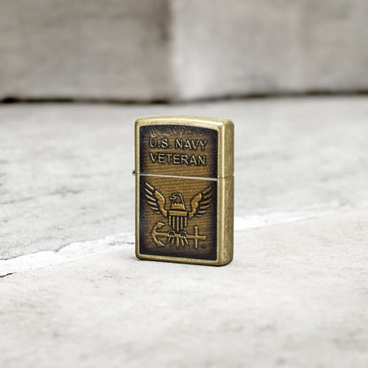 Lifestyle image of Zippo United States NavyÂ® Street Brass Windproof Lighter standing on a grey tile floor.