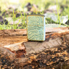 Lifestyle image of Zippo Map Armor High Polish Green Windproof Lighter sitting on a log.