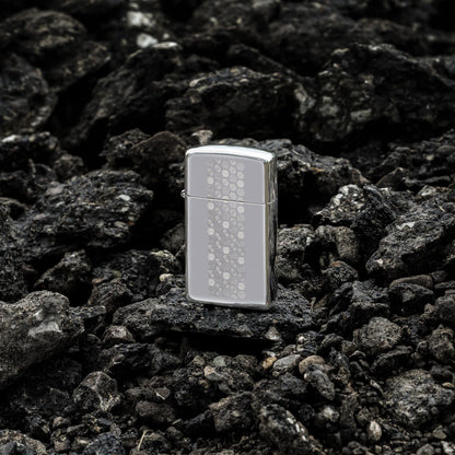 Lifestyle image of Zippo SlimÂ® Honeycomb Design High Polish Chrome Windproof Lighter standing on dark, loose rocks.