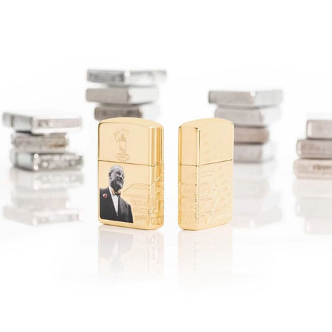 Lifestyle image of Zippo 2023 Founder's Day Collectible Armor High Polish Brass Windproof Lighters, standing in a white scene with Zippo lighters stacked behind them.