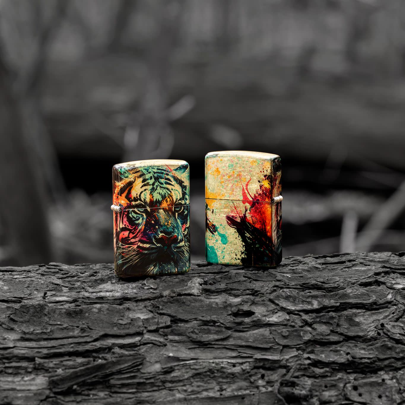 Lifestyle image of two Zippo Painted Tiger Design 540 Tumbled Brass Windproof Lighters standing on a log in a black and white scene.