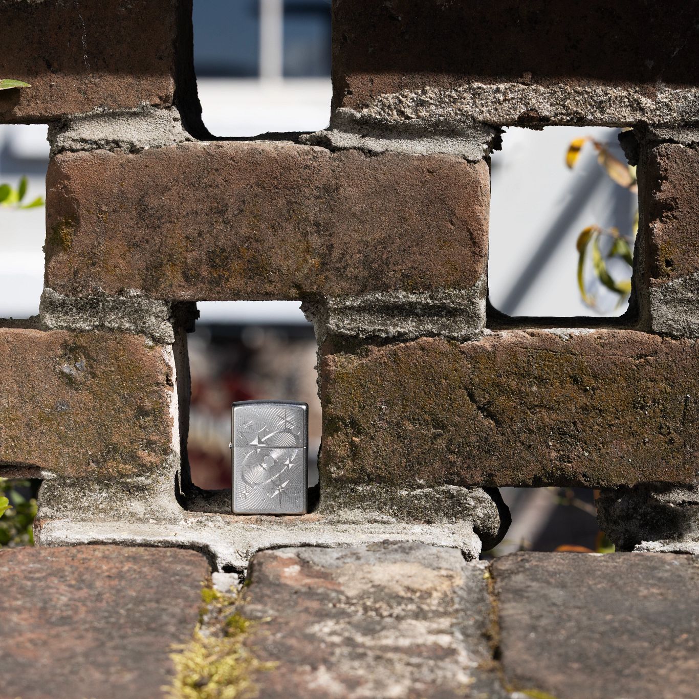 Lifestyle image of Zippo Atomic Cosmos Design Satin Chrome Windproof Lighter standing in a gap of a brick wall.