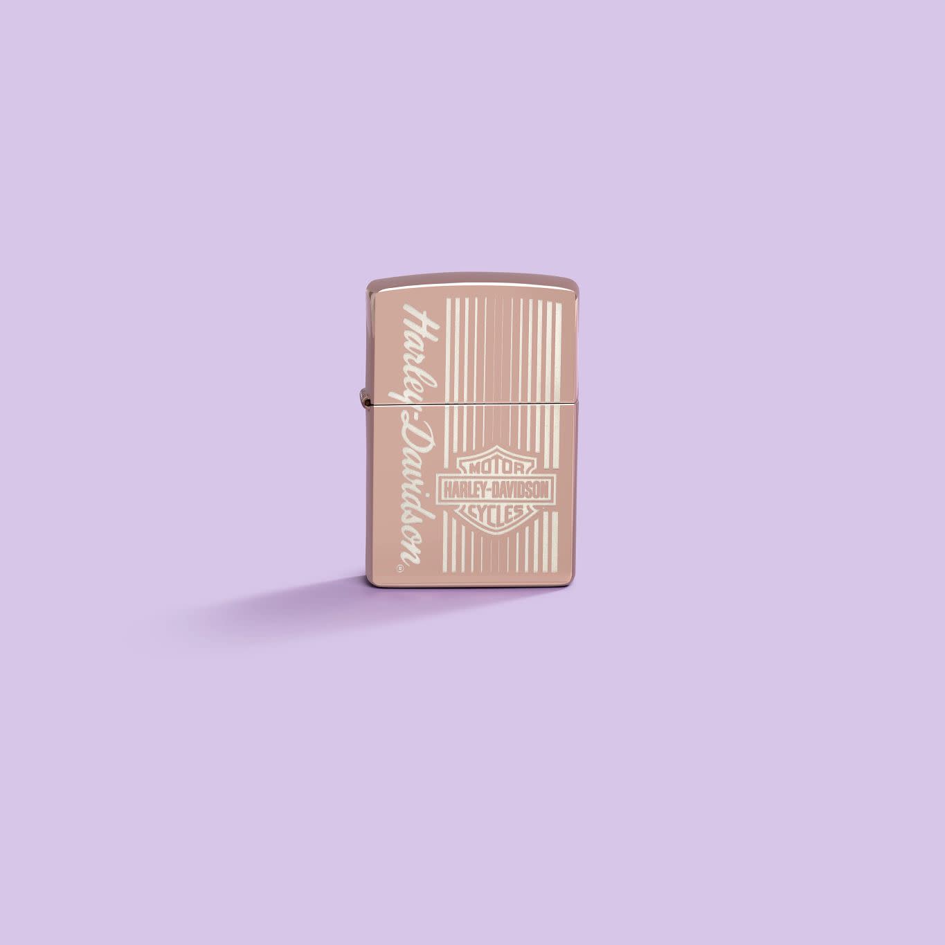 Lifestyle image of Zippo Harley-DavidsonÂ® High Polish Rose Gold Windproof Lighter on a pastel purple background.