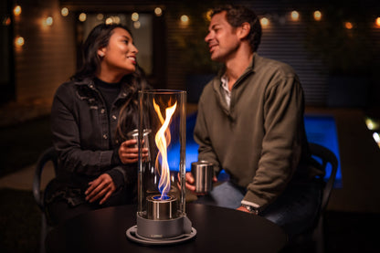 Lifestyle image of the Zippo FlameScapesâ„¢ Spiral Fire Feature XL in black, lit on a table with a cityscape and couple in the background.