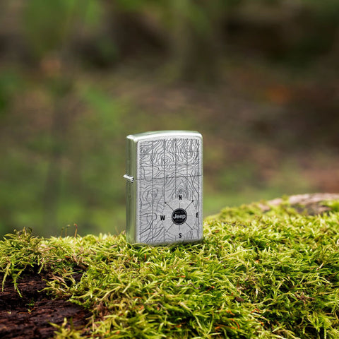 Lifestyle image of Zippo Jeep Topographical Map Street Chrome Windproof Lighter standing outside on a mossy log.