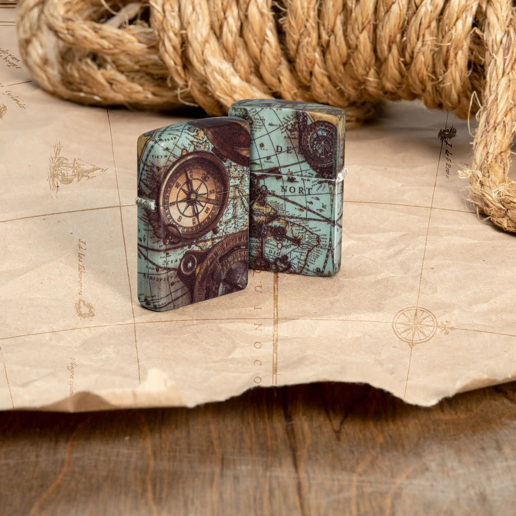 Lifestyle image of two Zippo Compass Design 540 Matte Windproof Lighters standing on an old map with a rope in the background.