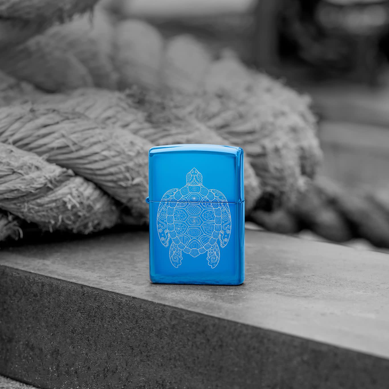 Lifestyle image of Zippo Zen Turtle Design High Polish Blue Windproof Lighter standing in front of a rope on a wooden plank.