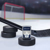 Lifestyle image of the NHL® Toronto Maple Leafs™ Street Chrome™ Windproof Lighter standing with a hockey puck and hockey stick, with a hockey net in the background.