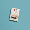 Lifestyle image of Chevy Vintage Corvette White Matte Windproof Lighter laying on a turquoise background.