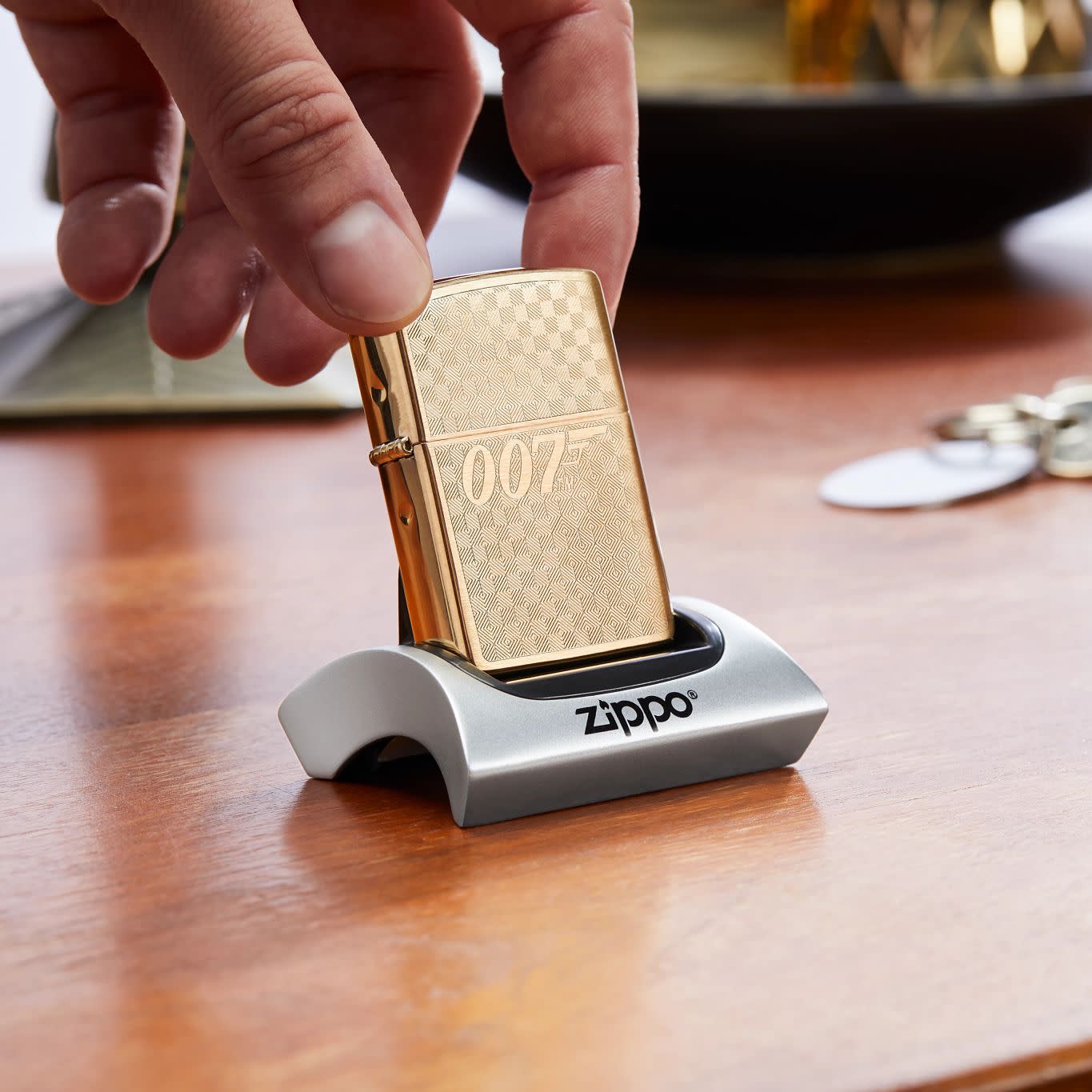 Lifestyle image of Zippo Textured James Bond 007â„¢ Design Brushed Brass Windproof Lighter sitting in a display stand on a desk.