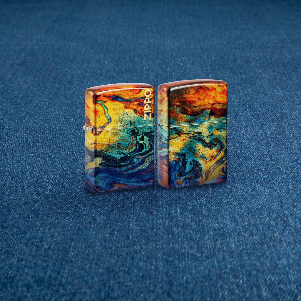 Lifestyle image of two Zippo Colorful Design 540 Tumbled Brass Windproof Lighters standing on a denim surface.
