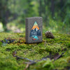 Lifestyle image of Zippo Mountain Design Iron Stone Windproof Lighter on a moss-covered rock in the woods.