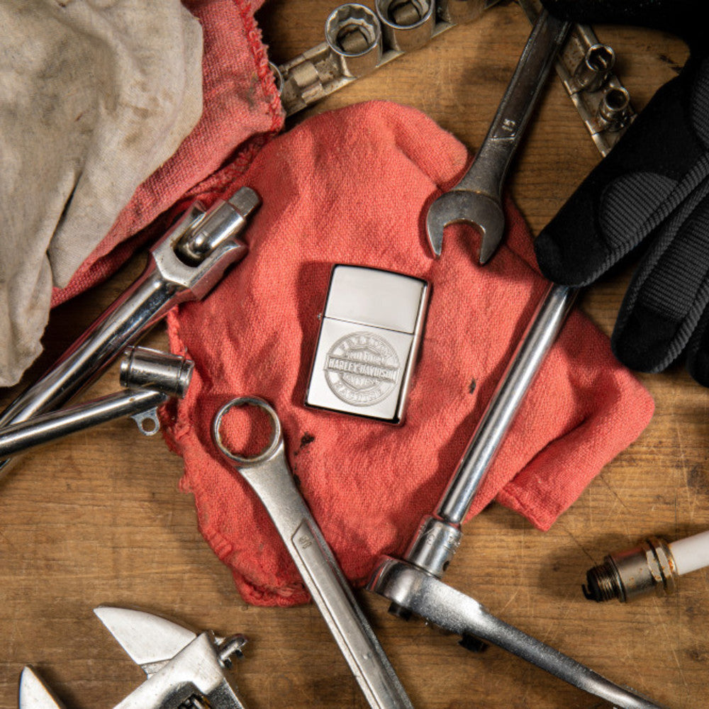 Lifestyle image of Harley-DavidsonÂ® Bar and Shield High Polish Chrome Windproof Lighter laying flat with tools surrounding it.