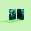 Lifestyle image of two Zippo Anne Stokes Collection 540 Tumbled Brass Windproof Lighters on a pastel green background.