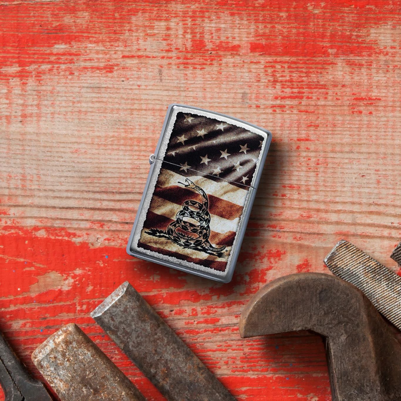 Lifestyle image of Zippo Dont Tread on MeÂ® Street Chrome Windproof Lighter laying on worn red painted wood with tools laying below.