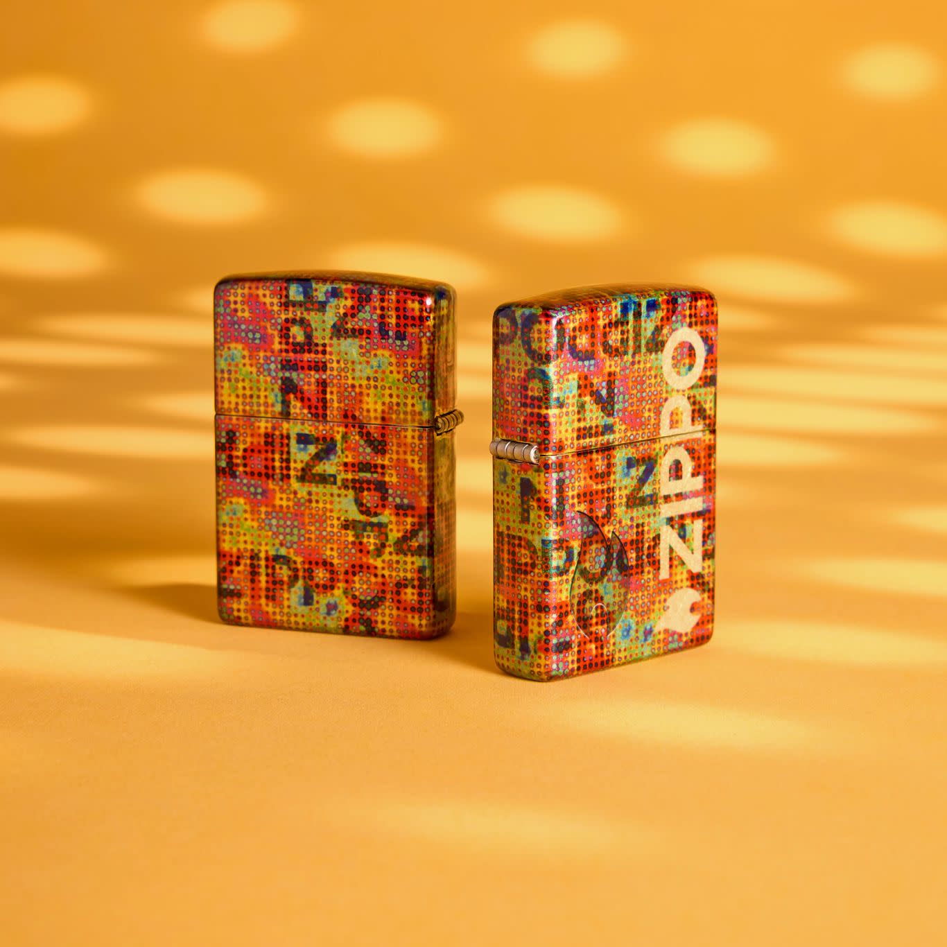 Lifestyle image of two Zippo Pixel Fusion Design 540 Tumbled Brass Windproof Lighters with a spotted orange background.