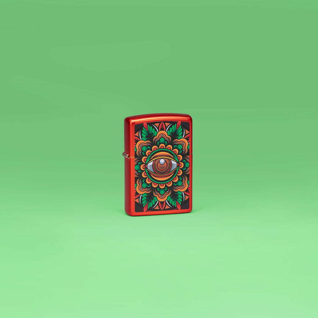 Lifestyle image of Zippo Counter Culture Eye Design Metallic Red Windproof Lighter standing in a green scene.
