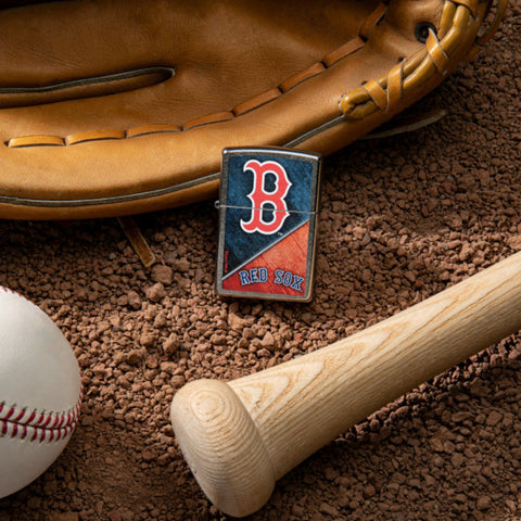 Lifestyle image of MLB® Boston Red Sox™ Street Chrome™ Windproof Lighter laying on a baseball field with a glove, ball, and bat.