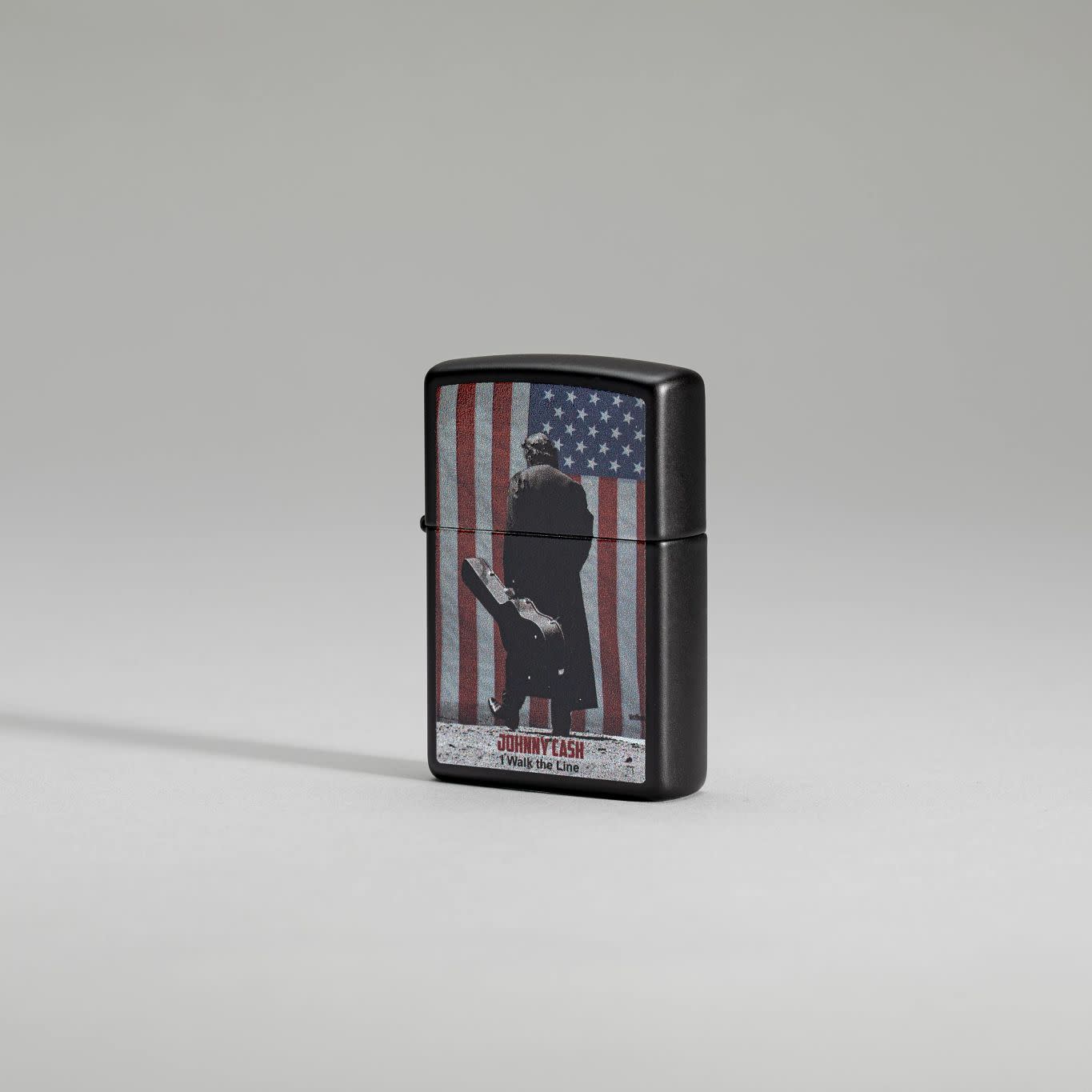 Lifestyle image of Zippo Johnny Cash Walk the Line Black Matte Windproof Lighter standing on a gray background.