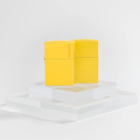 Lifestyle image of two Zippo Classic Sunflower Logo Windproof Lighters on a clear pedestal and a white background.