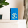 Lifestyle image of Zippo Seal Design Sky Blue Matte Windproof Lighter standing in front of a plant.