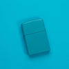 Lifestyle image of Classic Flat Turquoise Windproof Lighter laying on a turquoise surface