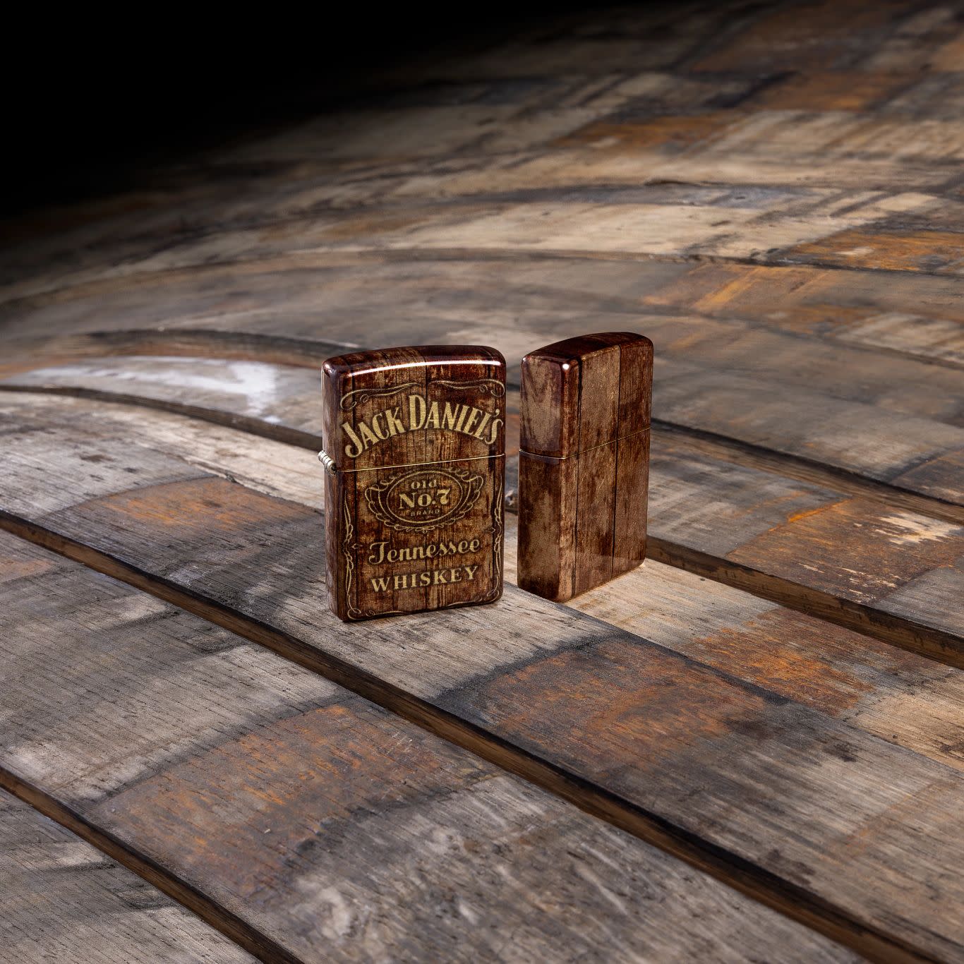 Lifestyle image of Zippo Jack Daniel'sÂ® Barrel Design 540 Tumbled Brass Windproof Lighter standing on a barrel.