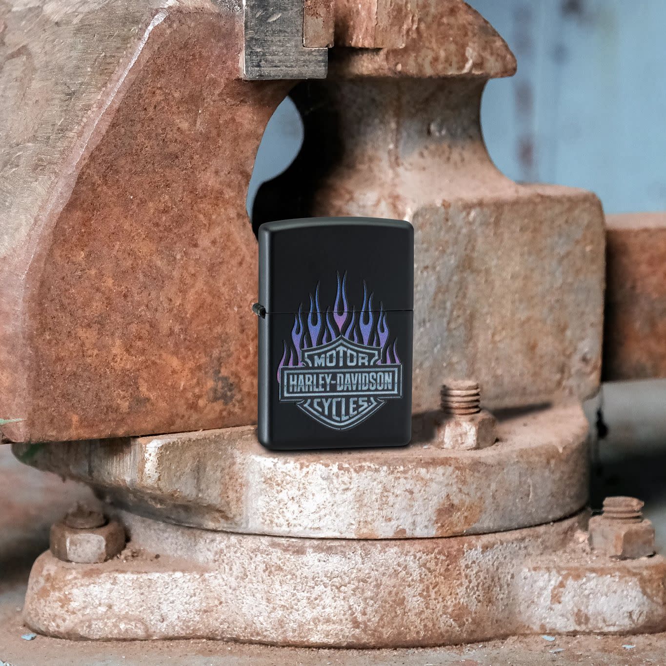 Lifestyle image of Zippo Harley DavidsonÂ® Flames Black Matte Windproof Lighter standing on a rusty vise.