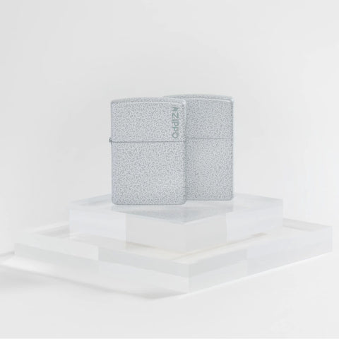 Lifestyle image of two Zippo Classic Glacier Logo Windproof Lighters on a clear pedestal and a white background.