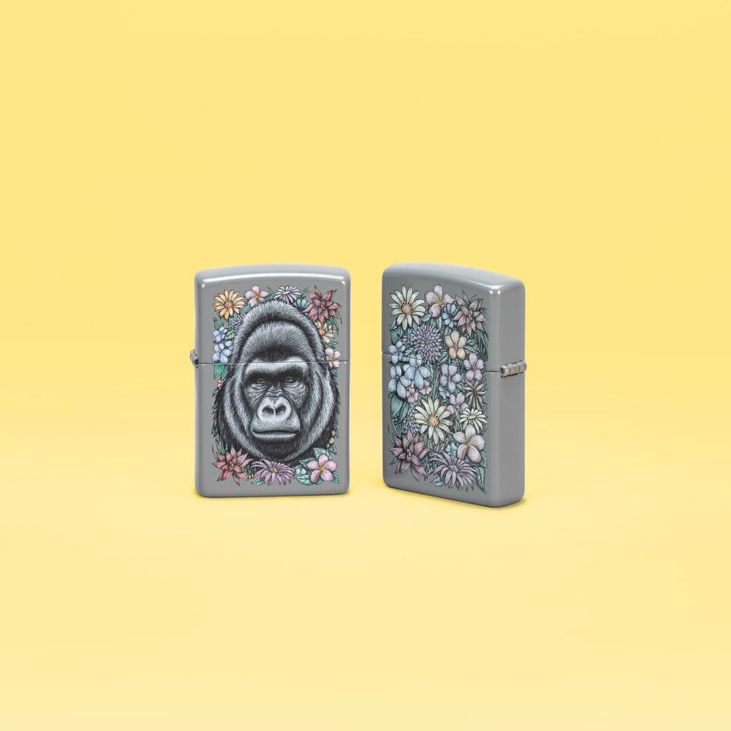 Lifestyle image of two Zippo Floral Gorilla Design Flat Grey Windproof Lighter standing in a yellow scene.