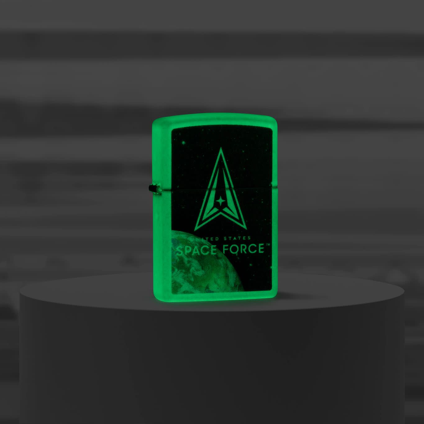 Lifestyle image of Zippo U.S. Space Forceâ„¢ Glow in the Dark Windproof Lighter standing on a pedestal glowing in the dark.