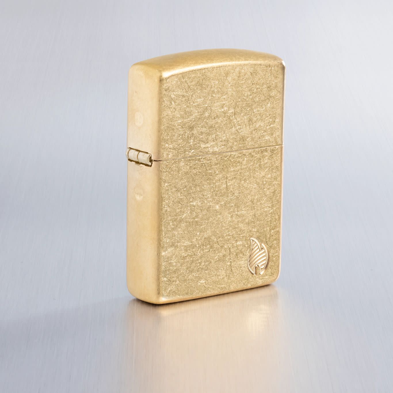 Lifestyle image of Zippo ArmorÂ® Series Flame Tumbled Brass Windproof Lighter on a light gray background.