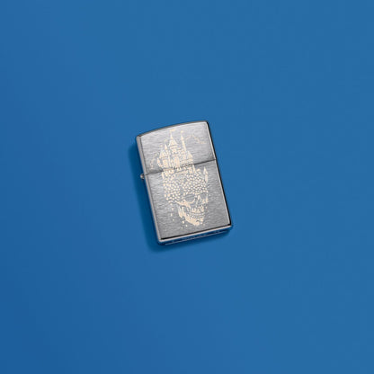 Lifestyle image of Zippo Skull Castle Design Brushed Chrome Windproof Lighter in a blue scene.