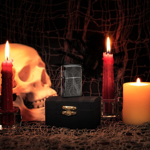 Lifestyle image of Rib Cage Design High Polish Black Windproof Lighter, standing on a chest with lit candles, a human skull, and a spider and web behind it.