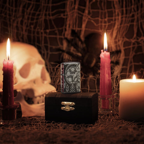 Lifestyle image of Occult Design High Polish Black Windproof Lighter, standing on a chest with lit candles, a human skull, and a spider and web behind it.